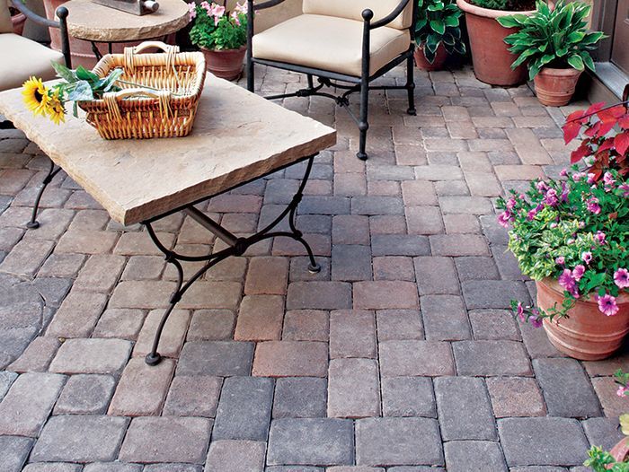 A DIY Stone Patio with a stone table, chairs, and plants on top of it.