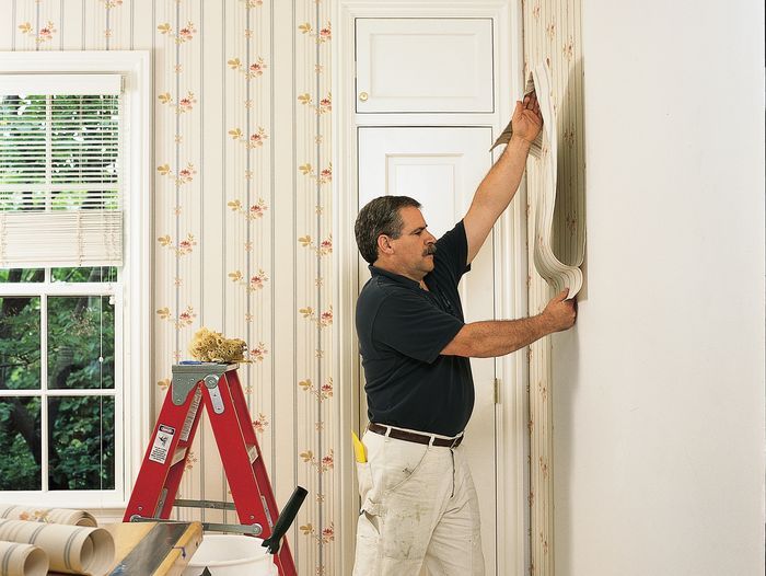 A man putting up a strip of wallpaper in front of a red ladder.