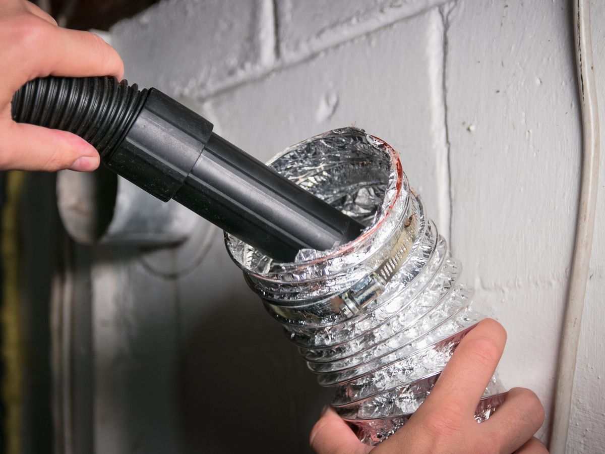 A person cleaning a dryer vent with a vacuum.