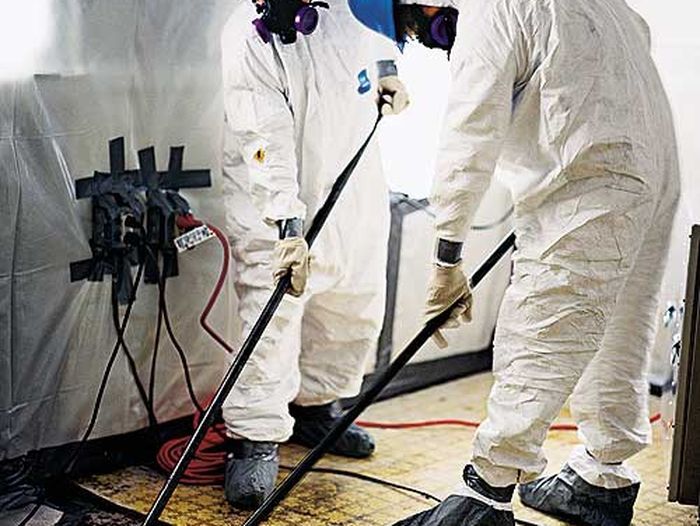 Two men in an asbestos abatement crew removing asbestos from the floor of a home.