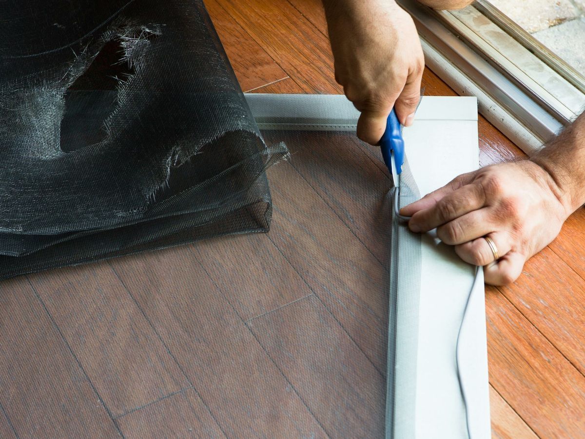 Person cutting a screen to size to replace a ripped screen door.