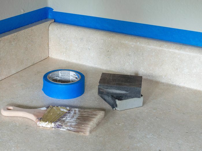 The supplies needed to prepare a laminate countertop, including a paint brush and blue tape.